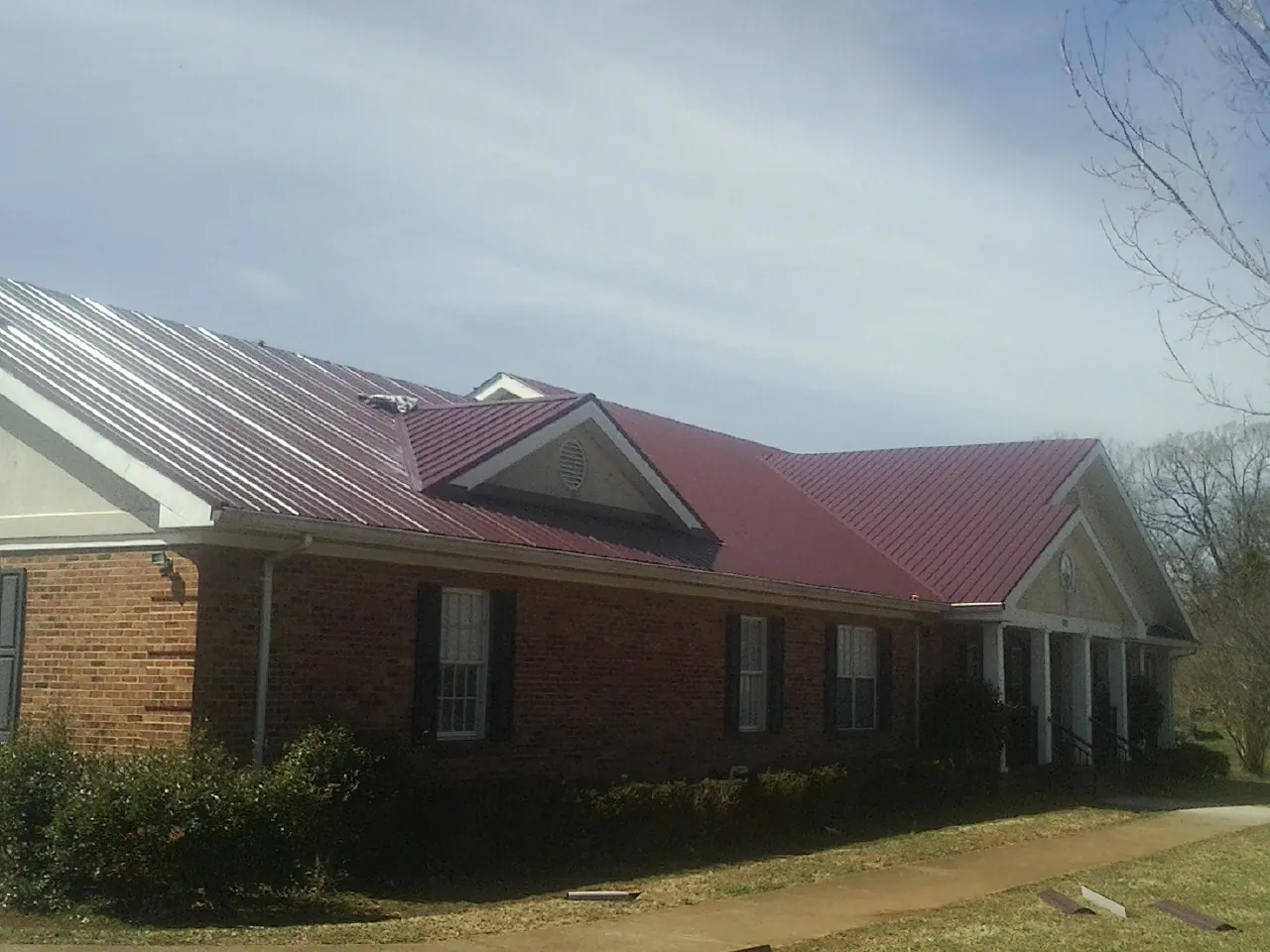 Red metal roof with gabled entries on a long brick building, from a Hail Damage Roof Repair job in Meriden