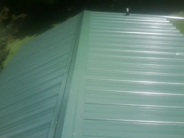 New green metal panels meeting at the ridge of a roof — Flat Roof Repair work by our crew in Meriden