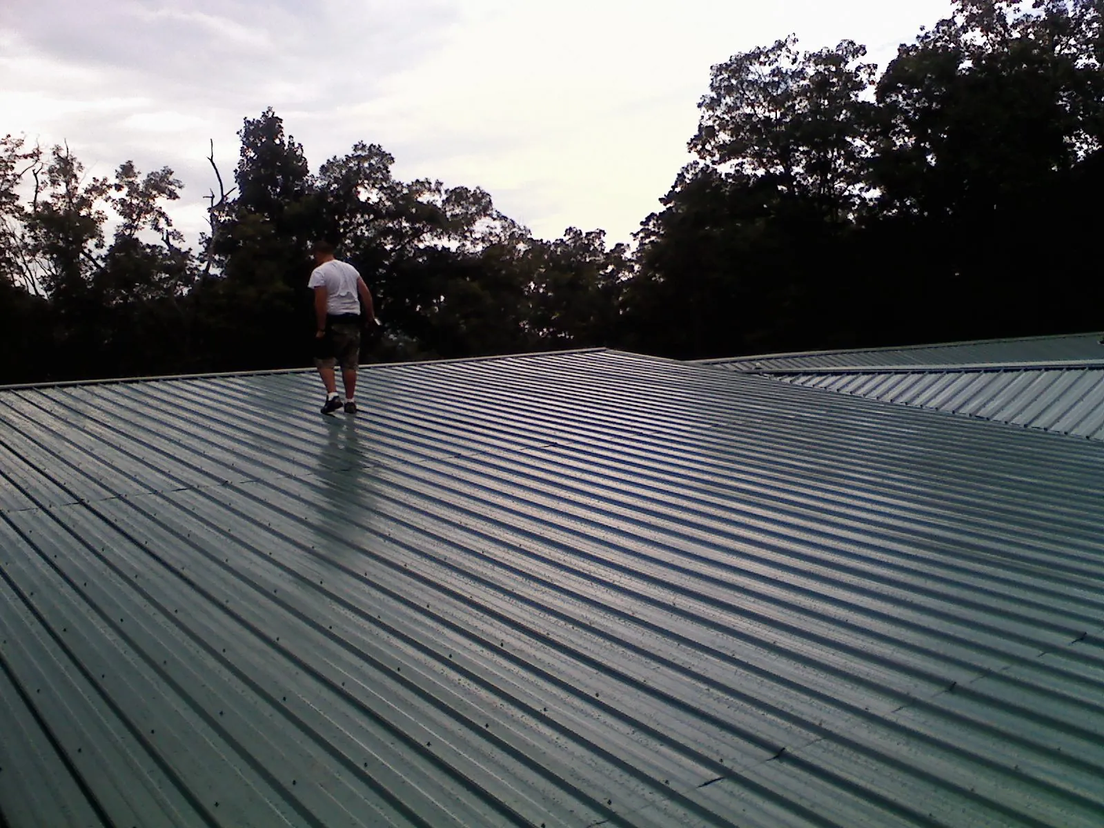 Roofer walking a wide expanse of new green metal roofing in Meriden