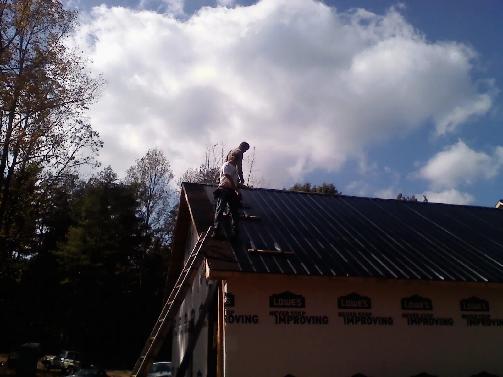 Roofer fastening dark metal panels high against a cloudy sky, from a Roof Inspection job in Meriden